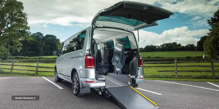 Silver wheelchair accessible vehicle with its rear ramp lowered in a countryside car park