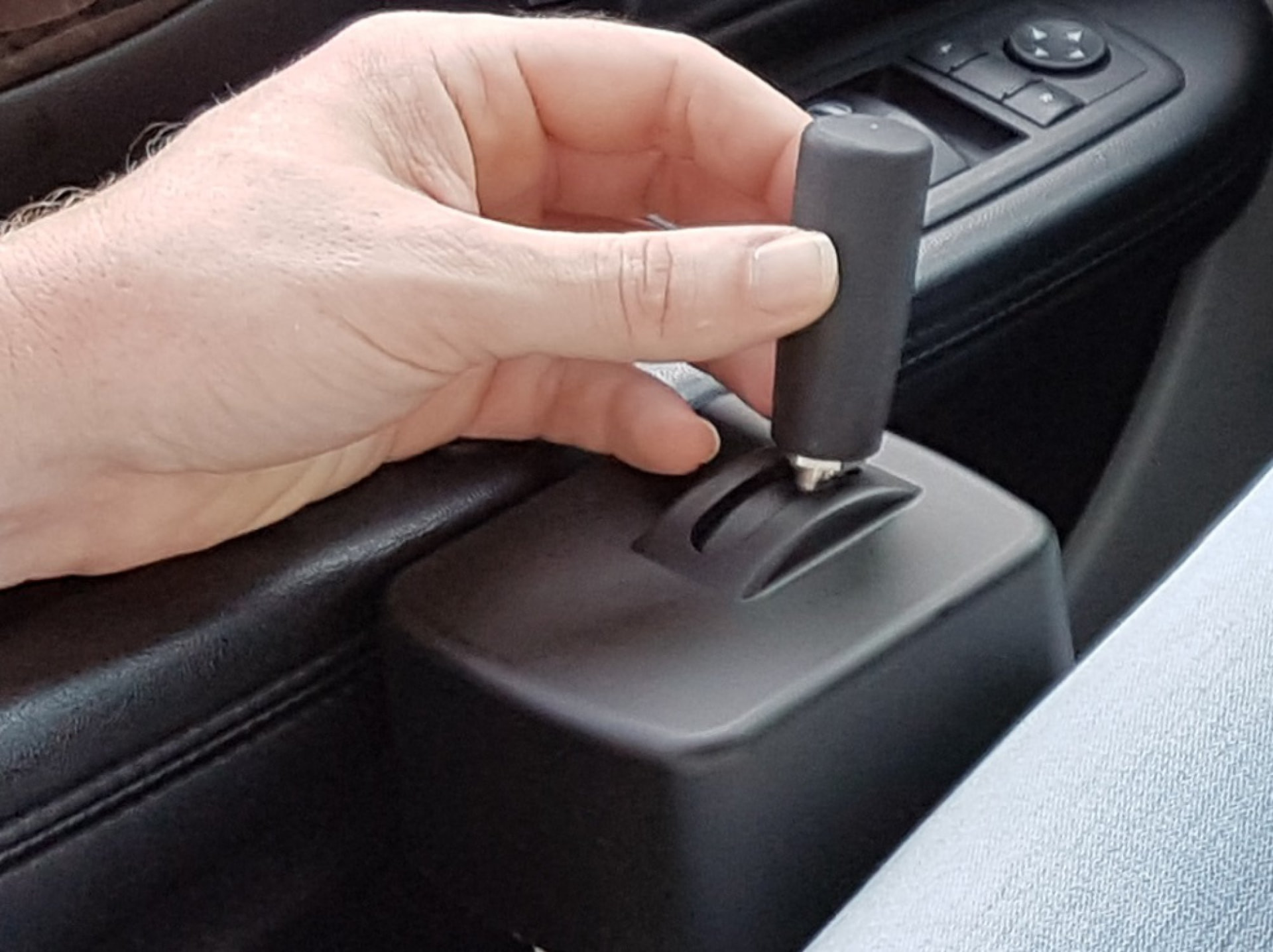Hand gripping a Bever gas and brake stick hand control fitted in a car